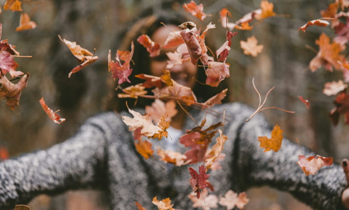 A blurry woman throwing autumn leaves into the air