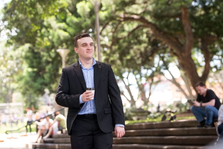 Open Universities Australia student Daniel, walking outside with a coffee.