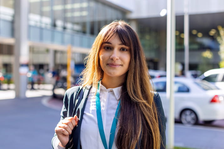 Open Universities Australia graduate, Adriana, in professional clothes, standing in front of South Metropolitan Health Service.