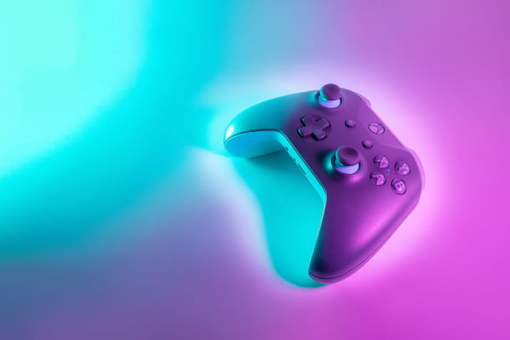 A gaming console controller on a neon lit background