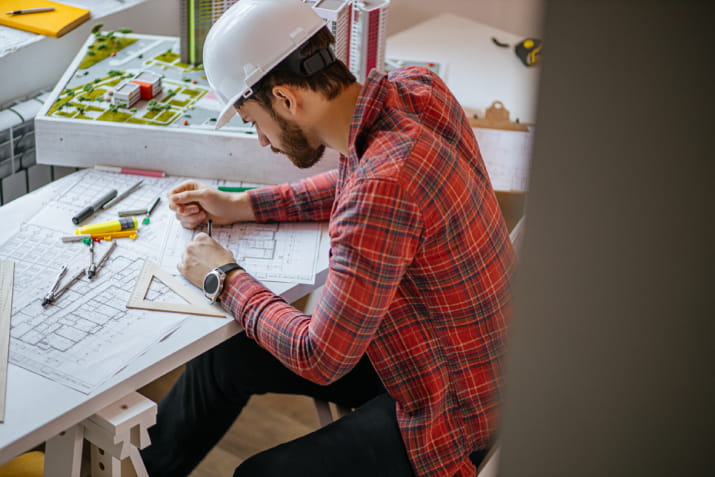 A person wearing hard hat while working on building project drawings.
