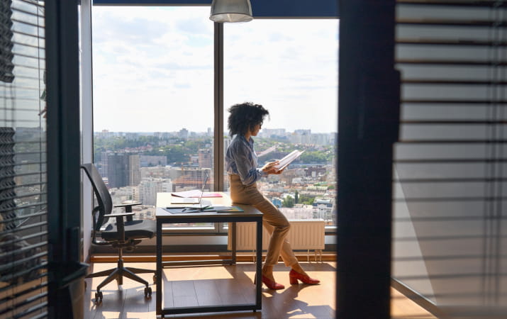 A woman leaning against a desk in an office with an impressive view