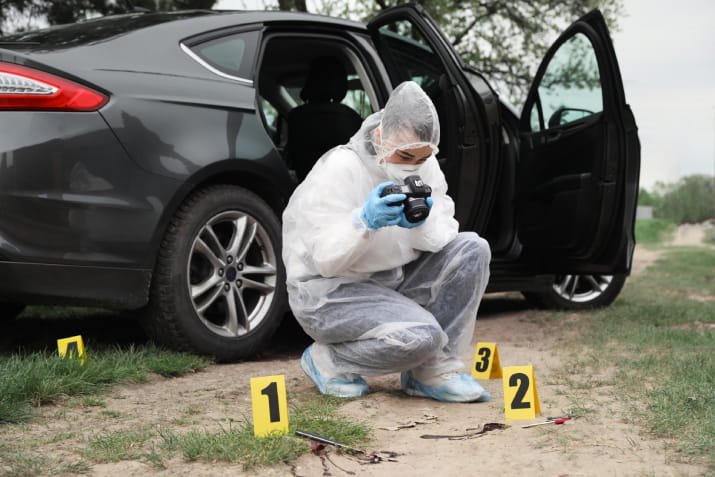 A forensics expert squatting and taking a photo at a crime scene