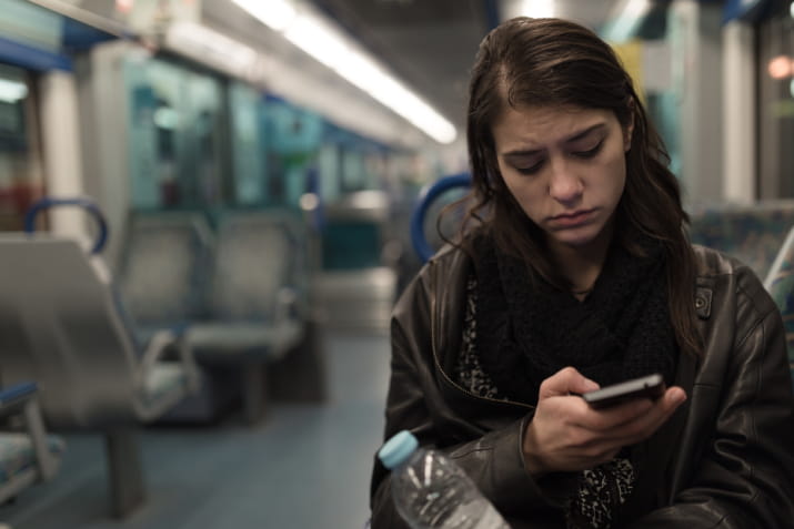 A sad young woman on a train looking at her phone