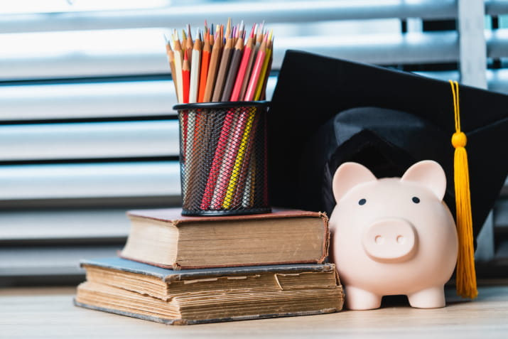 A piggy bank wearing a graduation cap set beside books and pencils