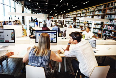 A busy library with stacks of books and people seated at workstations using computers